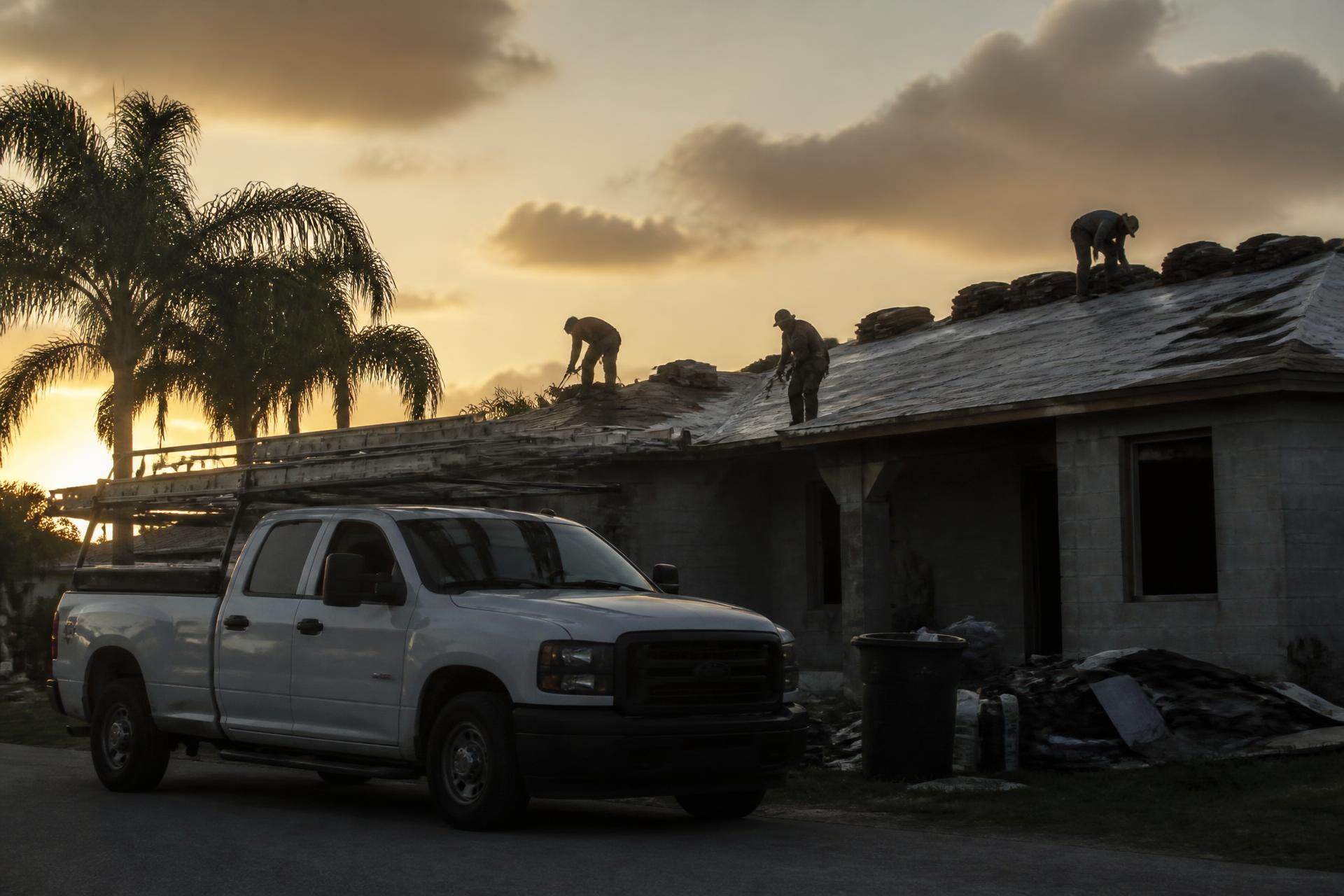Roofing crew working on a home at sunset with a work truck parked out front